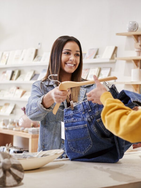 Female Sales Assistant In Independent Clothing And Gift Store Serving Female Customer Female Sales Assistant In Independent Clothing And Gift Store Serving Female Customer